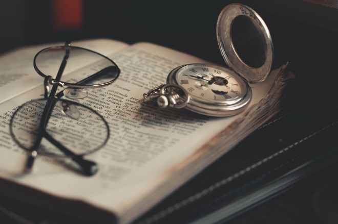 round silver colored pocket watch and eyeglasses on opened book